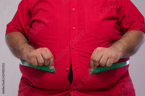 Close up of obese man measuring his overweight stomach with a measurement tape