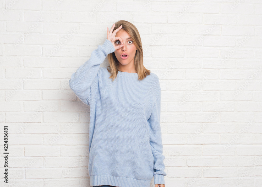 Beautiful young woman over white brick wall doing ok gesture shocked with surprised face, eye looking through fingers. Unbelieving expression. Beautiful young woman over white brick wall doing ok gesture shocked with surprised face, eye looking through fingers. Unbelieving expression.