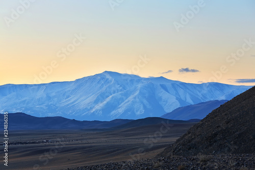 Highland river valley with yellow grass on a background of snow covered mountains and glaciers with beautiful sunrise. in the steppe near the mountains during the autumn, Western Mongolia
