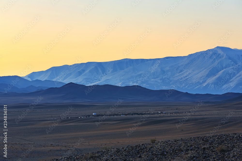Highland river valley with yellow grass on a background of snow covered mountains and glaciers with beautiful sunrise. in the steppe near the mountains  during the autumn, Western Mongolia