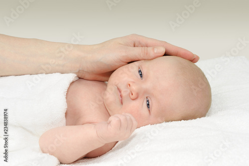 Baby boy lying on a white blanket and his mother's hand
