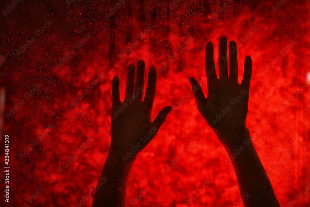 Female hands behind glass against red bloody background. Panic attack concept