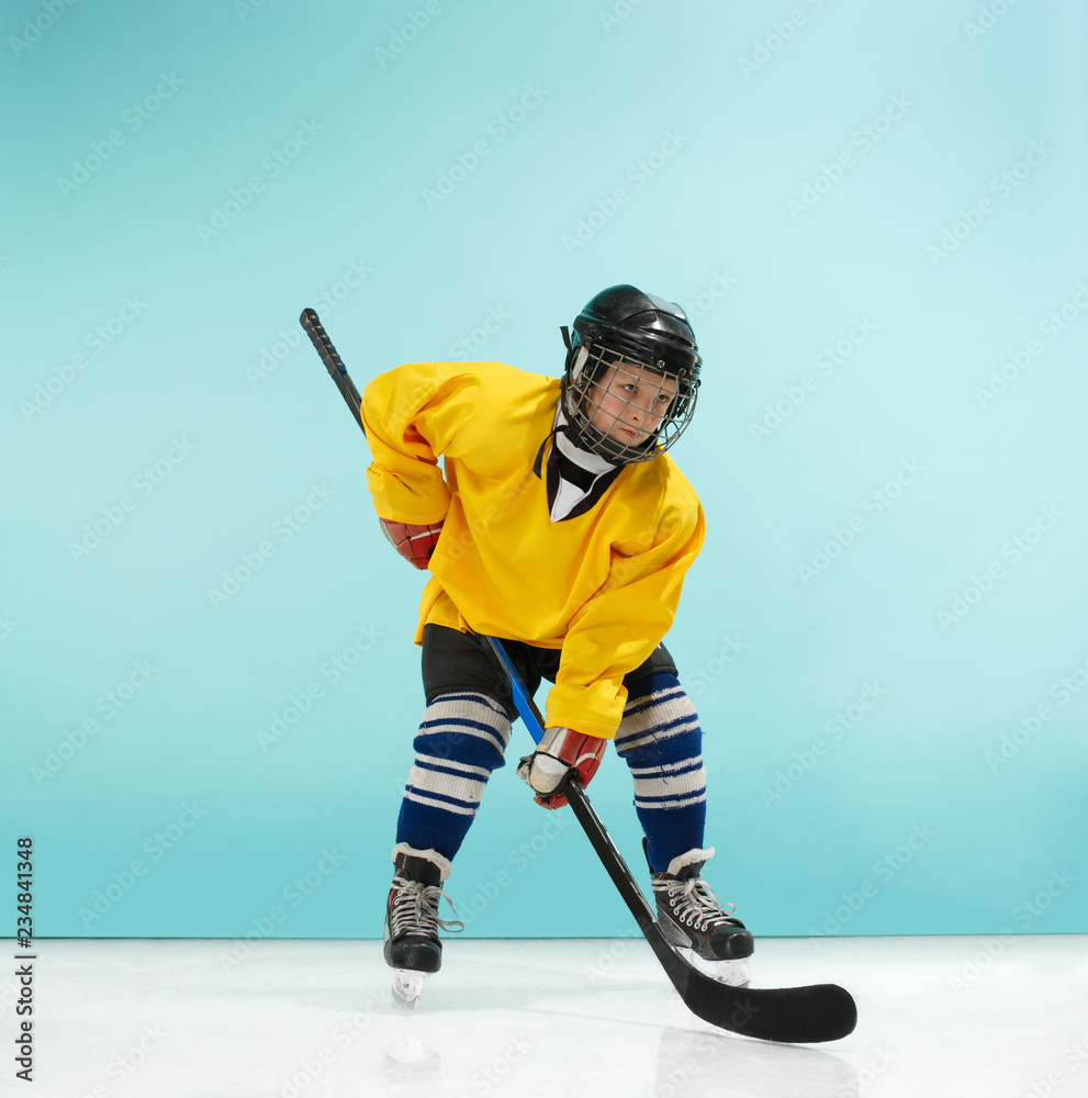 A hockey player in uniform with equipment over a blue studio background. The athlete, child, sport, action concept A hockey player in uniform with equipment over a blue studio background. The athlete, child, sport, action concept