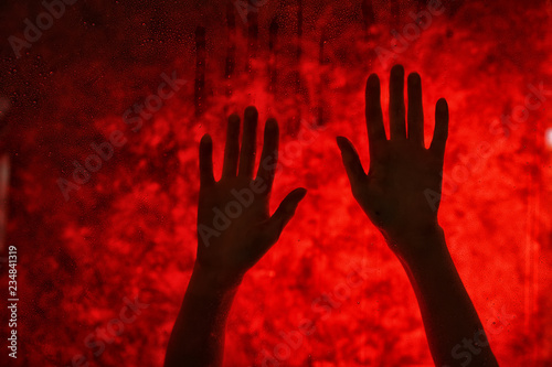 Female hands behind glass against red bloody background. Panic attack concept