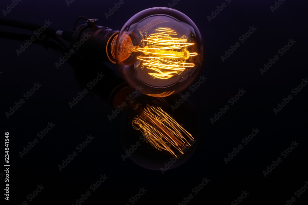 Glowing retro light bulb with reflection on black table