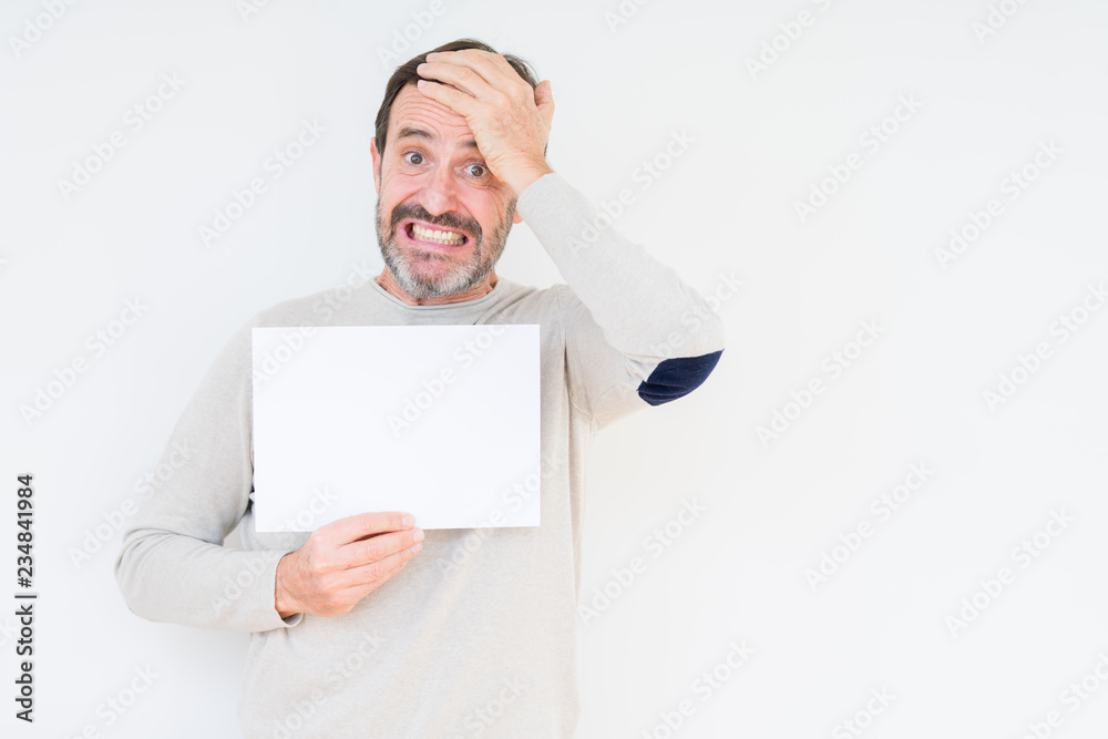 Senior man holding blank paper sheet over isolated background stressed with hand on head, shocked with shame and surprise face, angry and frustrated. Fear and upset for mistake. Senior man holding blank paper sheet over isolated background stressed with hand on head, shocked with shame and surprise face, angry and frustrated. Fear and upset for mistake.