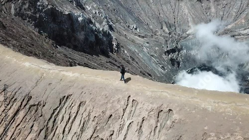 4K Tracking Couple walking by drone on adventure walkway at top of active Volcano with smoke at Mount Bromo (Pananjakan Peak) in Java island, Indonesia. Abstract for freedom life and creative. photo