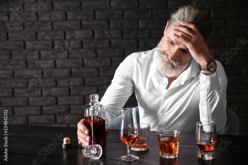 Depressed senior man drinki...