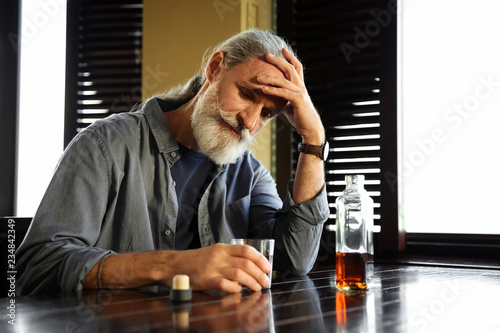 Depressed senior man drinki...