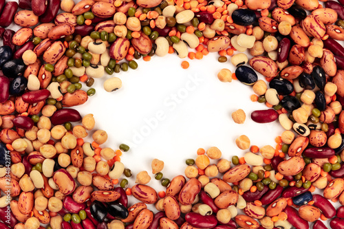 A photo of a mix of various types of legumes, shot from the top, forming a frame for copy space. Different beans, lentils, chickpeas, soybeans on a white background with a place for text