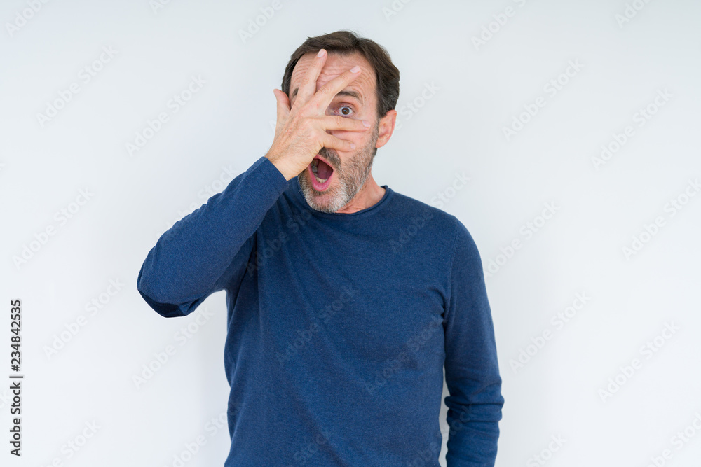 Elegant senior man over isolated background peeking in shock covering face and eyes with hand, looking through fingers with embarrassed expression. Elegant senior man over isolated background peeking in shock covering face and eyes with hand, looking through fingers with embarrassed expression.