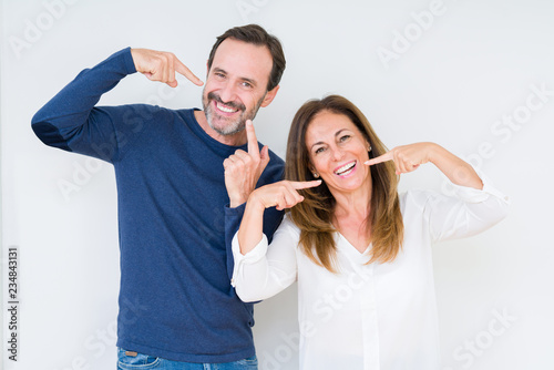 Beautiful middle age couple in love over isolated background smiling confident showing and pointing with fingers teeth and mouth. Health concept.