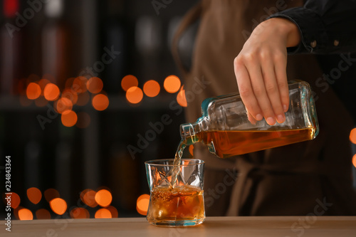 Foto Female bartender pouring whiskey from bottle into glass on table