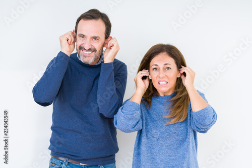 Beautiful middle age couple in love over isolated background Smiling pulling ears with fingers, funny gesture. Audition problem