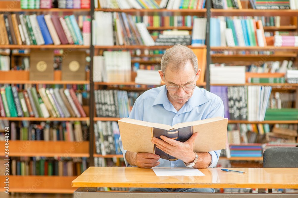 Senior man reading a book in the library. Empty space for text Senior man reading a book in the library. Empty space for text