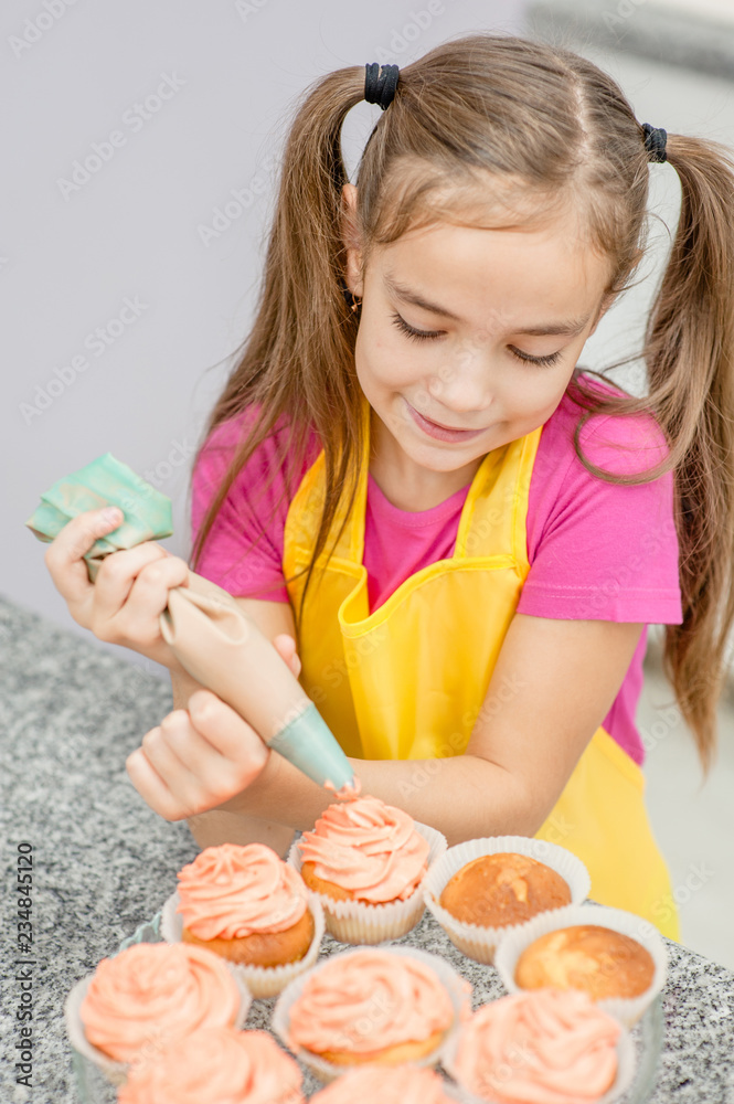little girl with confectionery bag squeezing cream on cupcakes at kitchen little girl with confectionery bag squeezing cream on cupcakes at kitchen