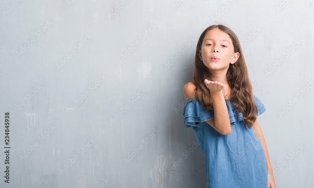 Obraz premium Young hispanic kid over grunge grey wall looking at the camera blowing a kiss with hand on air being lovely and sexy. Love expression.