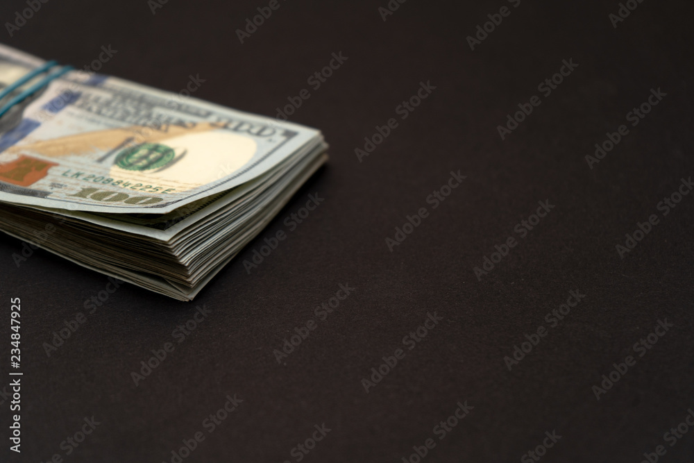 A pack of hundred dollar bills left on a black background A pack of hundred dollar bills left on a black background
