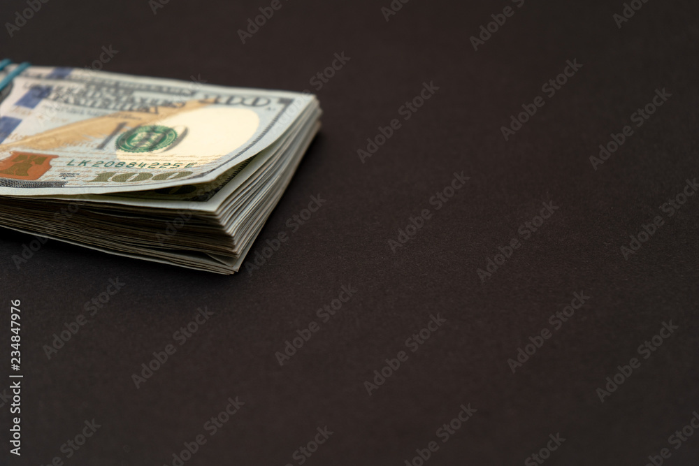A bundle of hundred dollar bills left on a black background A bundle of hundred dollar bills left on a black background