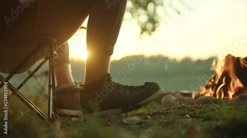 Close up of hikers feet in trekking boots near bonfire at sunset