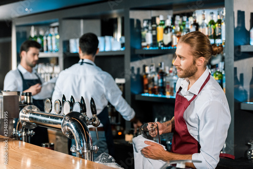 thoughtful barman polishing glass with cloth at wooden counter