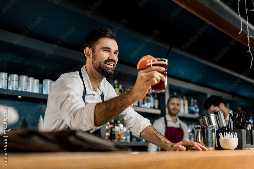 smiling bartender serving cocktail at wooden counter smiling bartender serving cocktail at wooden counter
