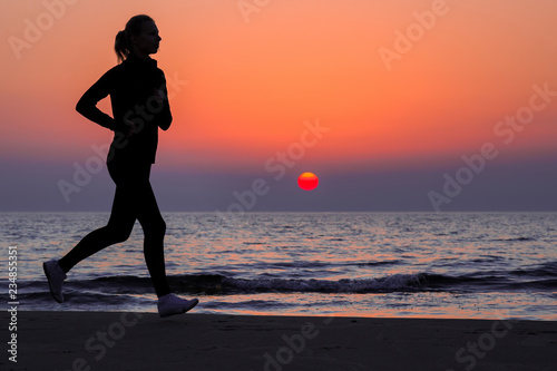 Alone woman running on sand beach. Beautiful red sunset. Enjoying sport in evening. Copy space. Empty place for motivational, inspirational text, quote or sayings on sky background. Side view.