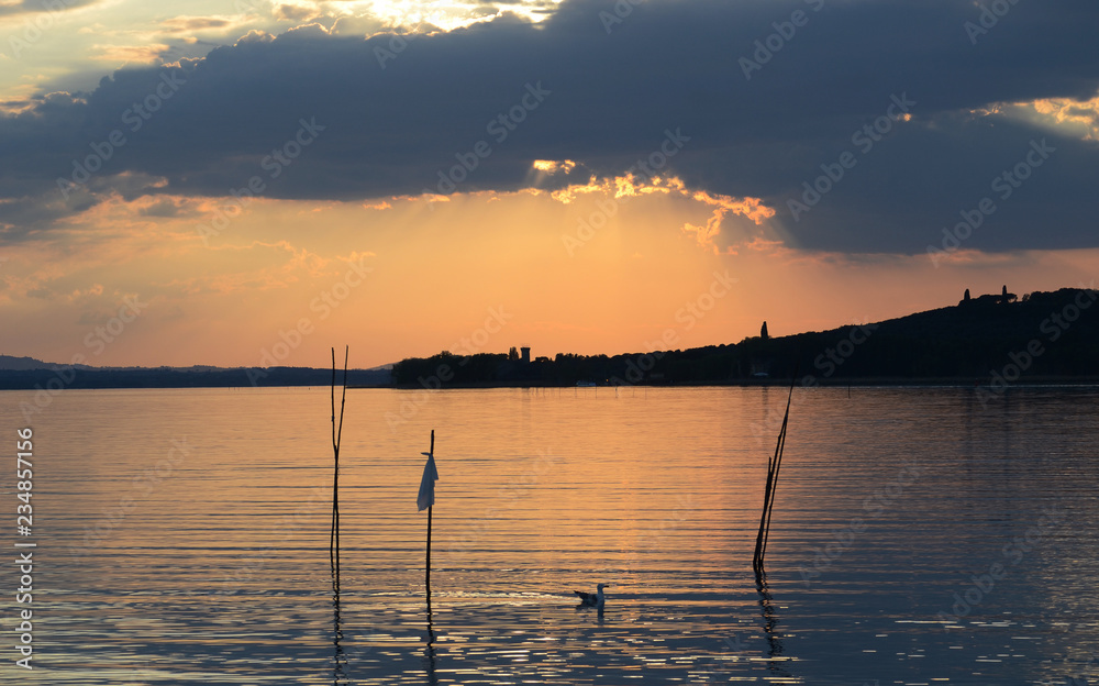 Umbria, Italy, landscape of Trasimeno lake at sunset, with Isola Polvese in background on a cloudy summer day