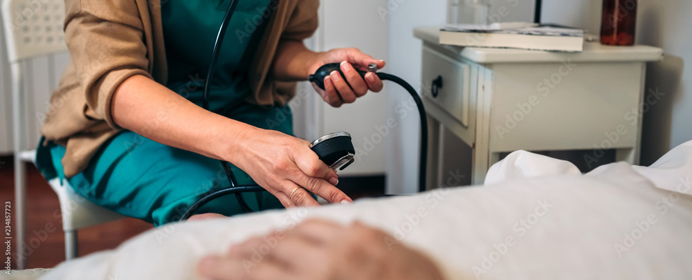 Female caregiver checking blood pressure to a senior woman at home