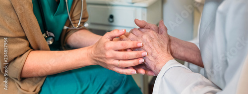 Female doctor giving encouragement to elderly patient by holding her hands photo