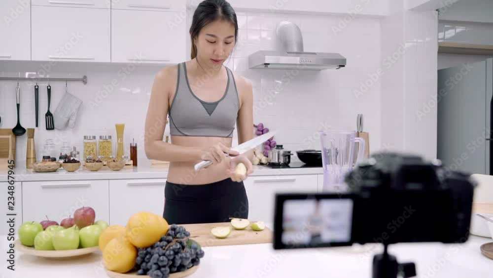 Blogger sporty Asian woman using camera recording how to make apple juice video for her subscriber, female use organic fruit making apple juice by herself at home. Healthy food concept. Blogger sporty Asian woman using camera recording how to make apple juice video for her subscriber, female use organic fruit making apple juice by herself at home. Healthy food concept.