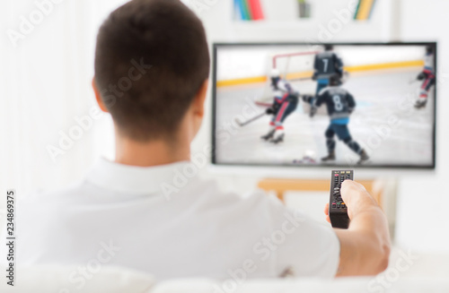 Photography leisure, sport and entertainment concept - man with remote watching ice hockey g