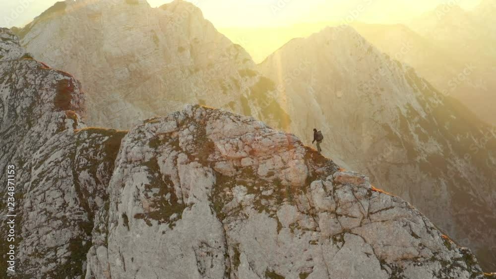Aerial view of man hiking on mountain top ridge at sunrise on dangerous climb.