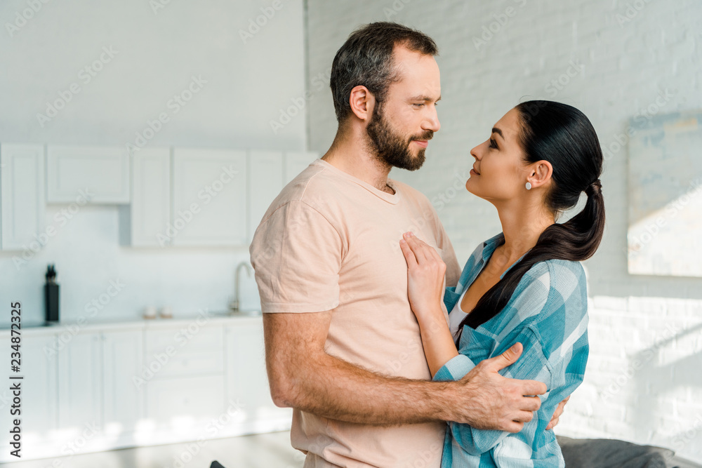 portrait of smiling couple embracing and looking at each other at home