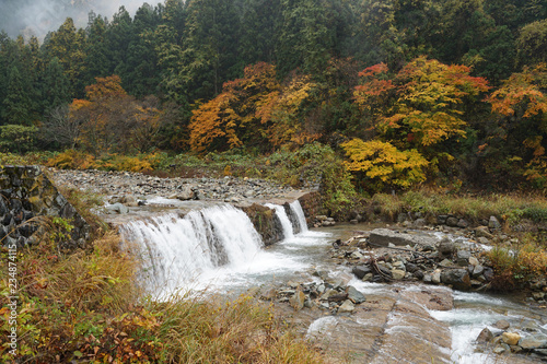 Beautiful autumn landscape of waterfall with large rocks and mountain background