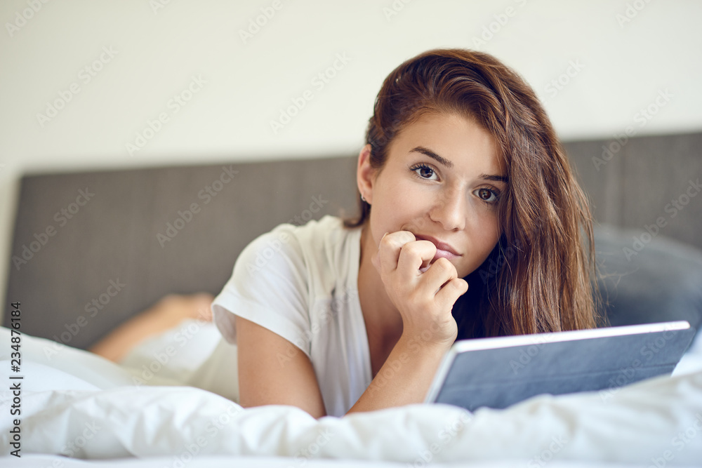Gelangweilte Frau liegt mit ihrem Tablet PC im Bett Gelangweilte Frau liegt mit ihrem Tablet PC im Bett