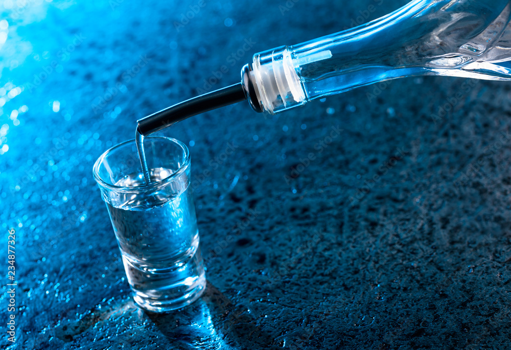 Vodka poured into a glass lit with blue backlight. Vodka poured into a glass lit with blue backlight.