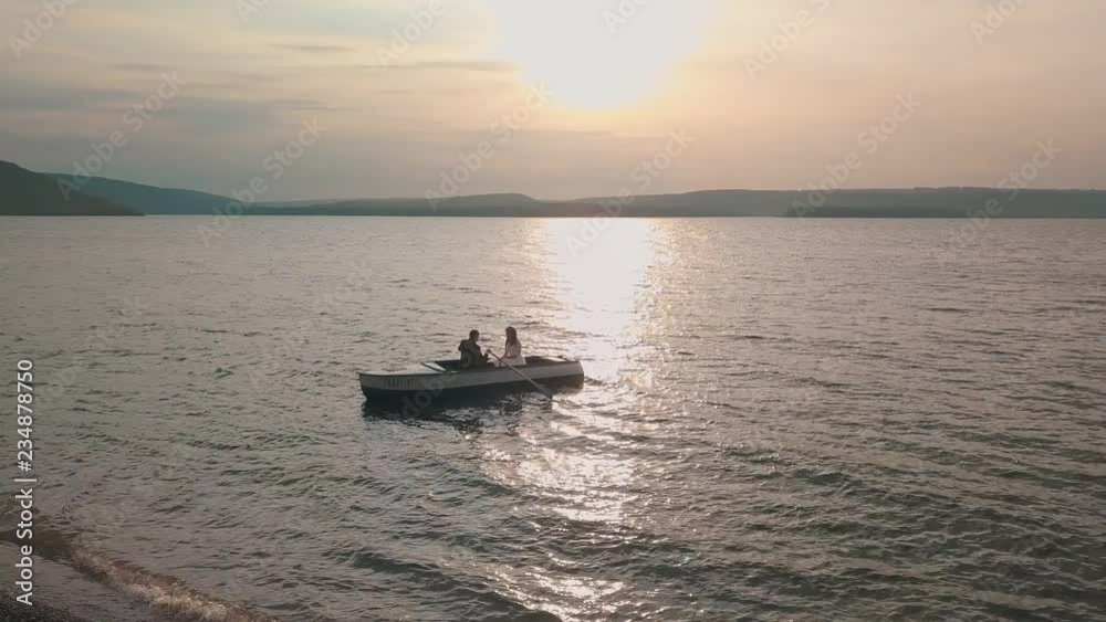 Young and beautiful wedding couple together sailing on a boat with oars on the sea. Sunset. Lovely groom and bride. Shooting from the air. Aerial shot Young and beautiful wedding couple together sailing on a boat with oars on the sea. Sunset. Lovely groom and bride. Shooting from the air. Aerial shot