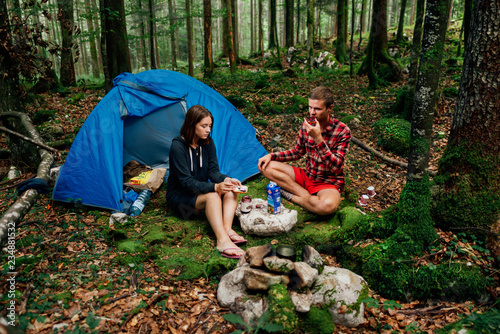 girl with a guy sitting near a tent in the woods and eat