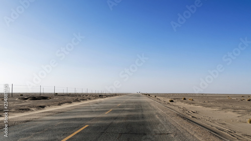 Asphalt road in the desert, strong winds blow up the sands across the road like wave.