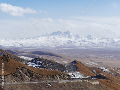 Scenic winter view from the asphalt road in the mountains covered with snow on a background of blue sky and clouds, road to snow mountain. photo