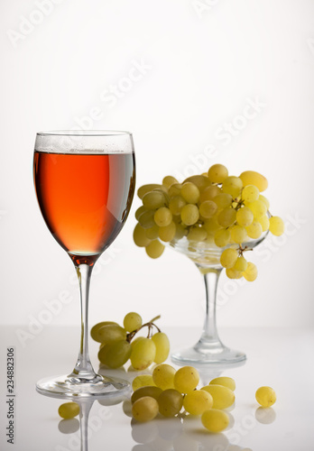 glass of wine and a bunch of ripe grapes on white background