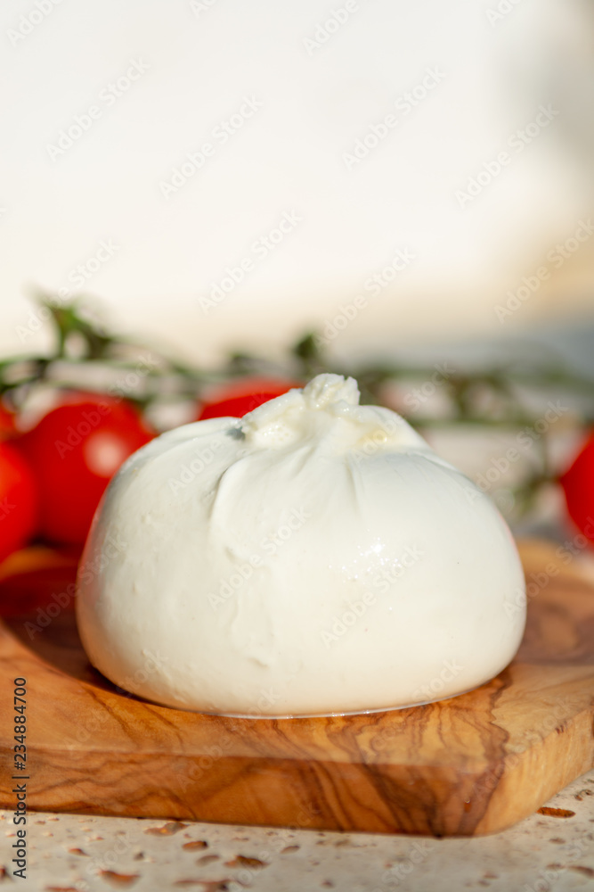 Fresh soft white burrata, buttery cheese, made from a mix of mozzarella and cream, original from Apulia region, Italy with tomatoes