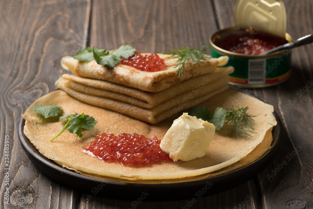Traditional russian dish - thin pancakes with red caviar and open tin can with caviar on the background Traditional russian dish - thin pancakes with red caviar and open tin can with caviar on the background