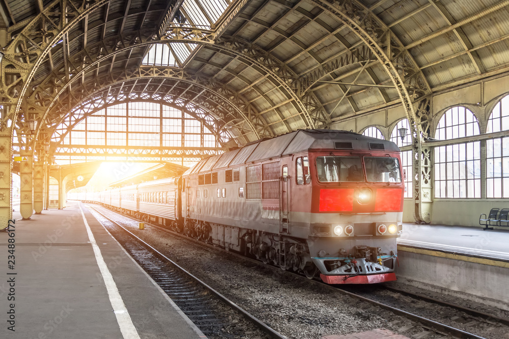 Obraz premium Pociąg pasażerski z lokomotywą spalinową na stacji pod dachem.