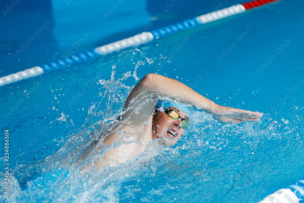Image of athlete man in blue cap swimming in style of crawl in swimming pool