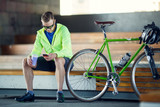 Photo of man in sunglasses with glass and phone in hands sitting on bench next to bicycle