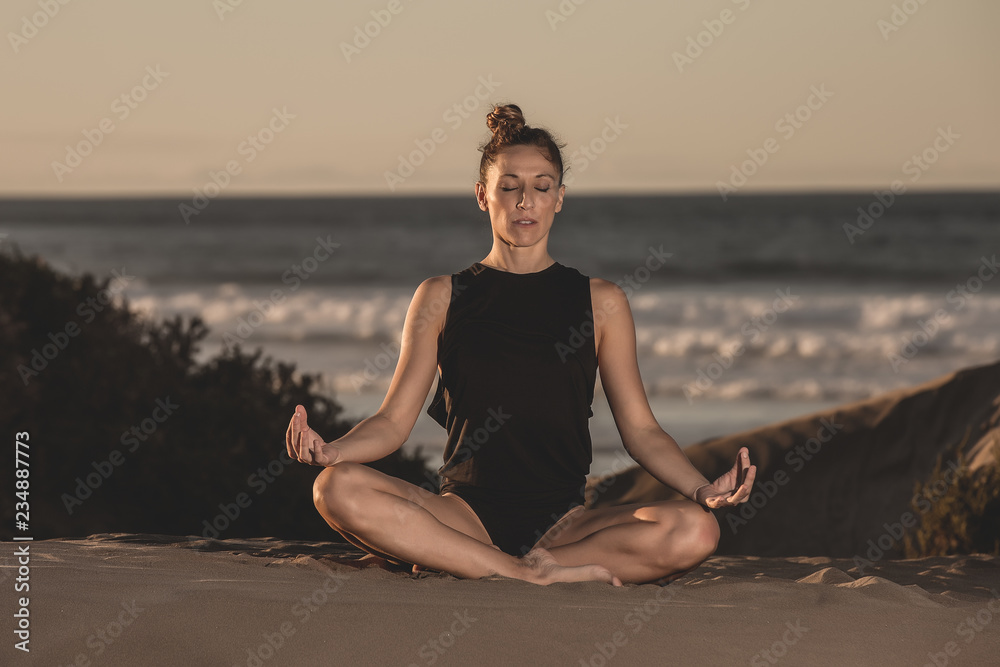 Meditating woman in bodysuit on beach