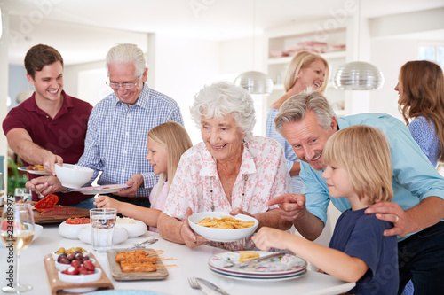 Multi-Generation Family And Friends Eating Food In Kitchen At Celebration Party