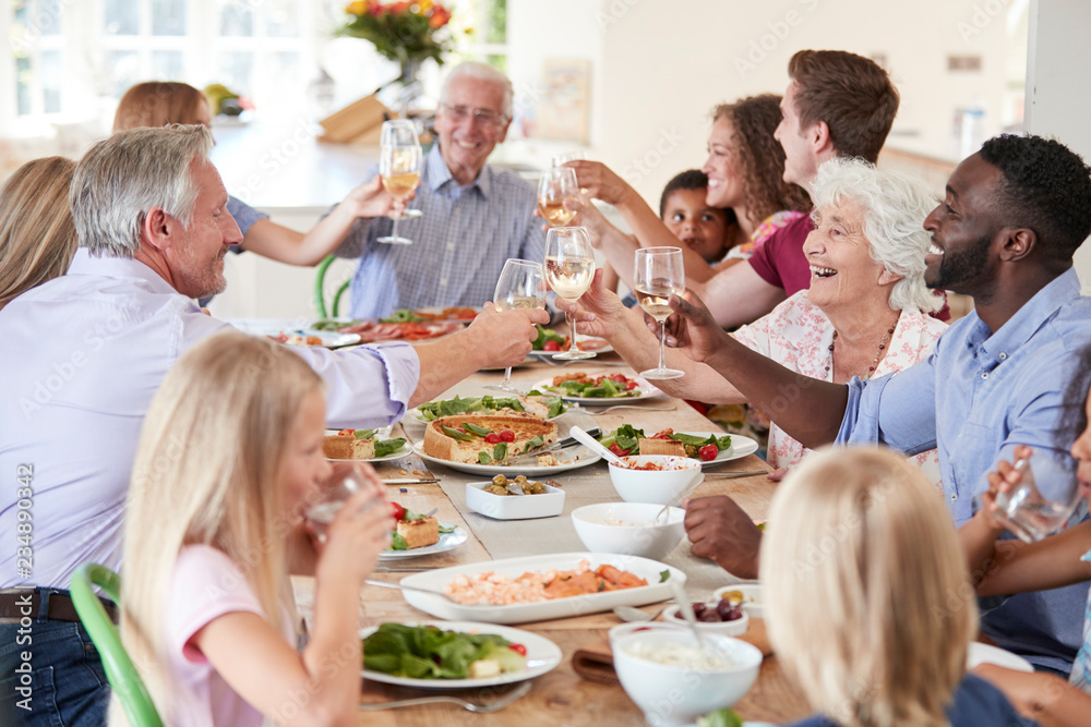 Group Of Multi-Generation Family And Friends Sitting Around Table And Making A Toast Group Of Multi-Generation Family And Friends Sitting Around Table And Making A Toast